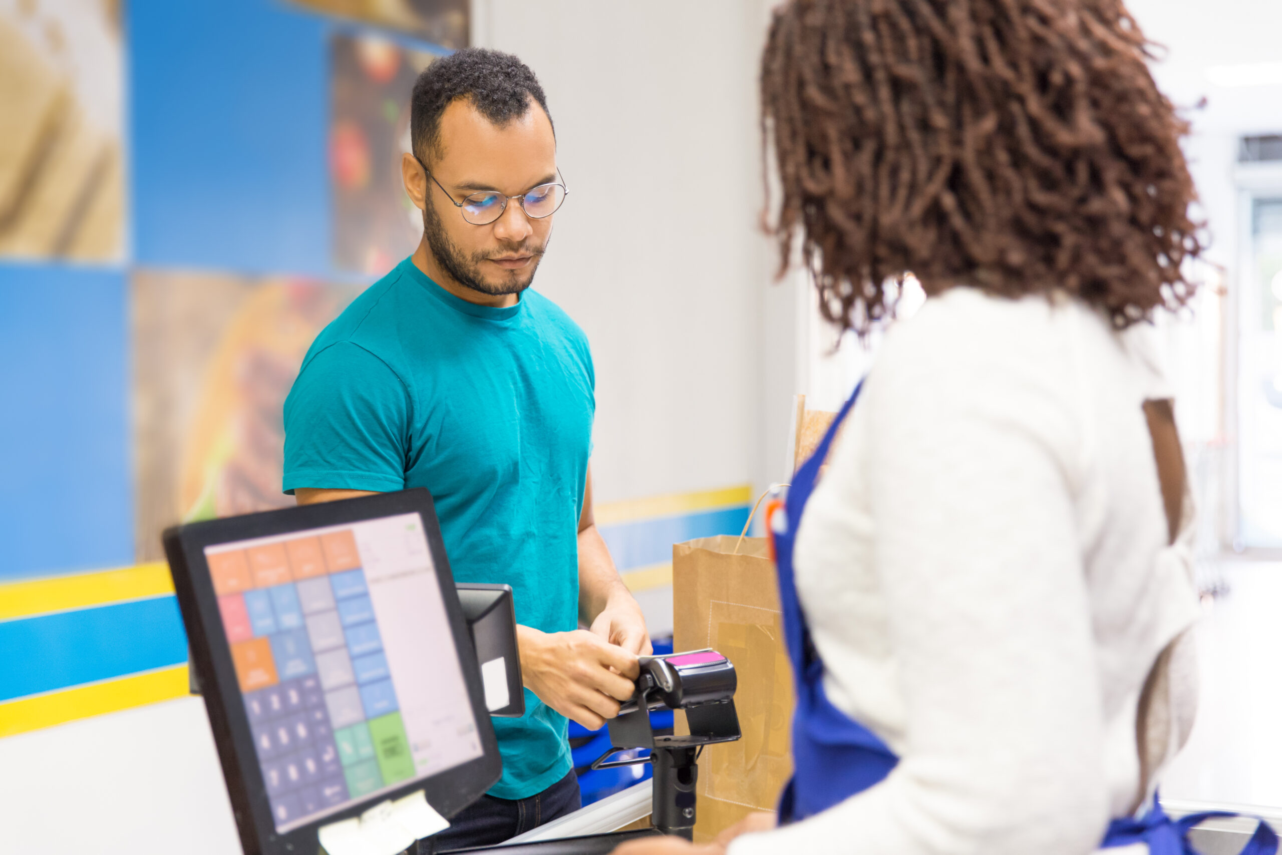 Focused young man paying bill in store. Back view of cashier standing at workplace. Shopping concept